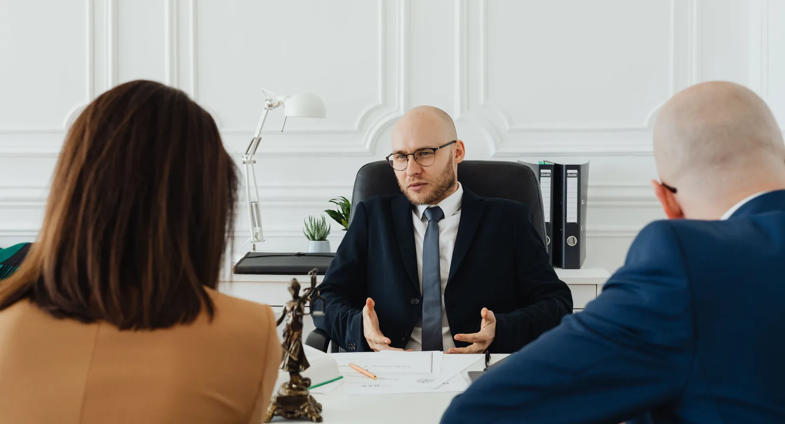 A business attorney meeting with two clients across a desk to discuss their legal needs