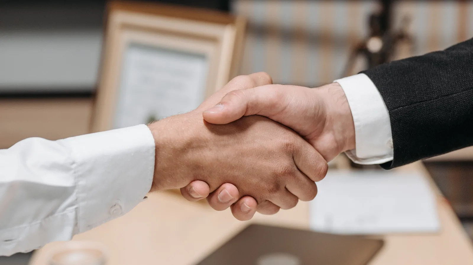 Two people shaking hands over a business purchase agreement and contract