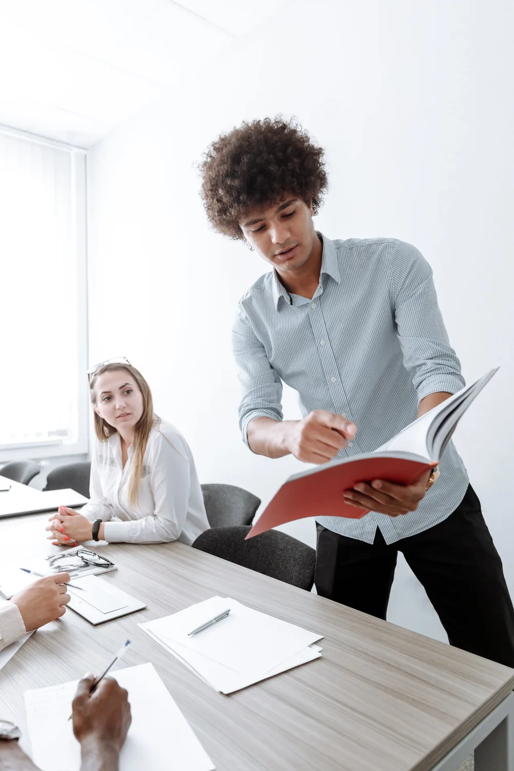 A manager reviews a printed policy document with two colleagues during a workplace meeting