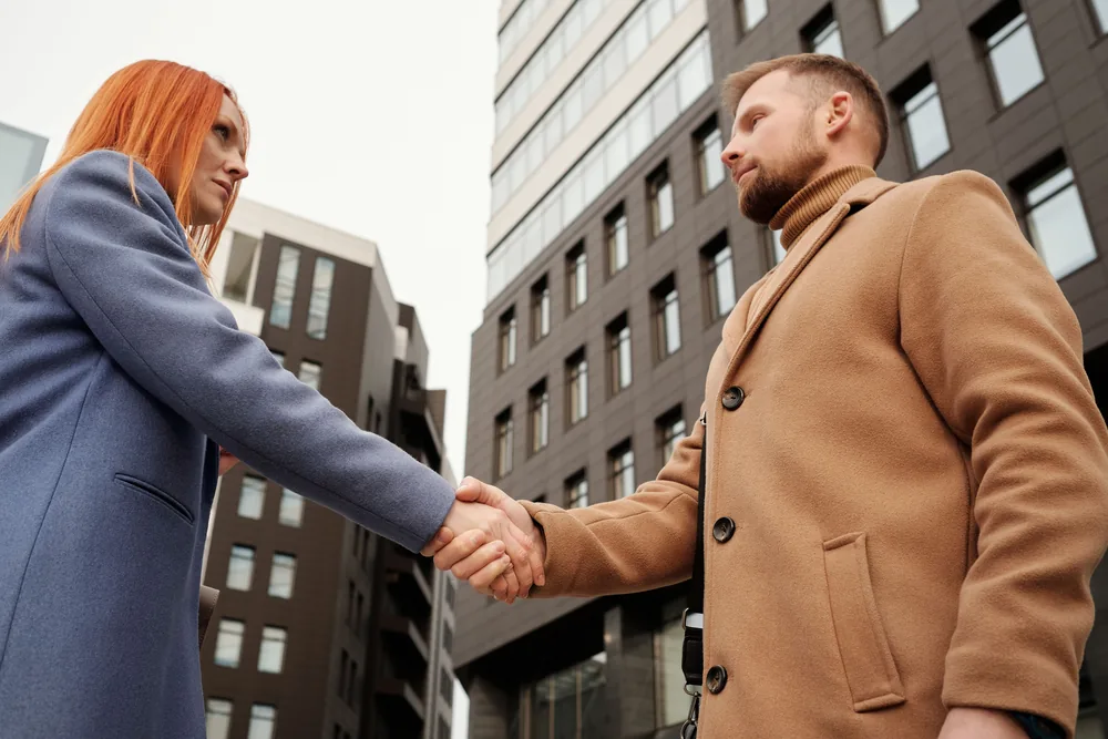 Two business partners shaking hands outside an office building after agreeing to work together