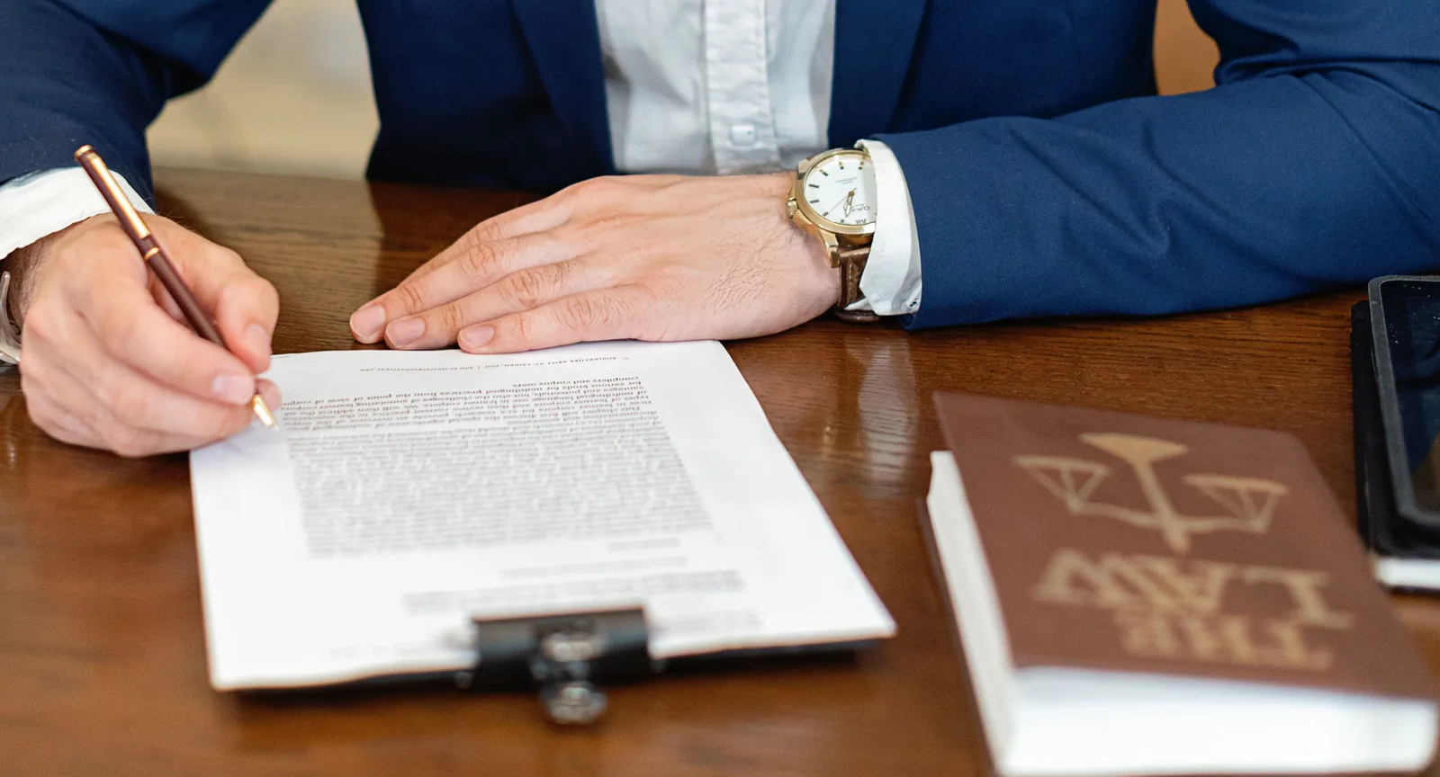 A professional in a navy suit signing a business contract beside a law book, illustrating SaaS contract review